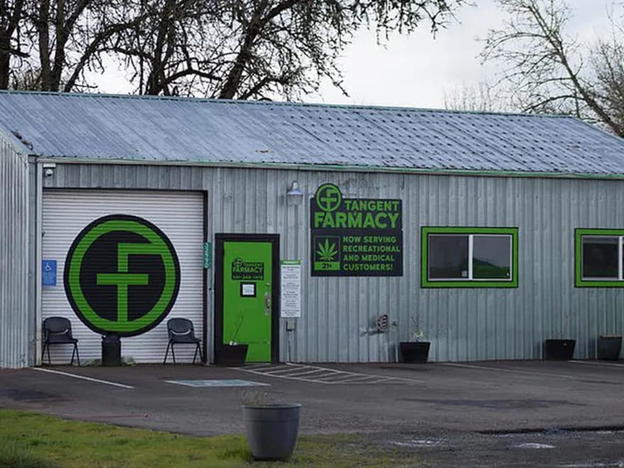 Tangent Farmacy storefront in Oregon, metal-clad exterior with the Tangent Farmacy logo painted on the rolling door and the green entry door.