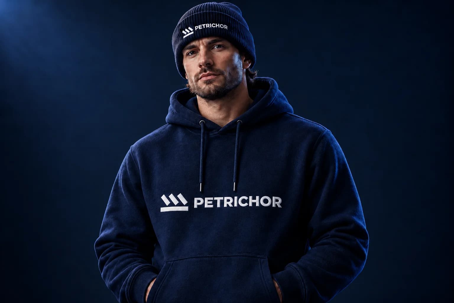 A person wearing a navy Petrichor hoodie and matching branded beanie.