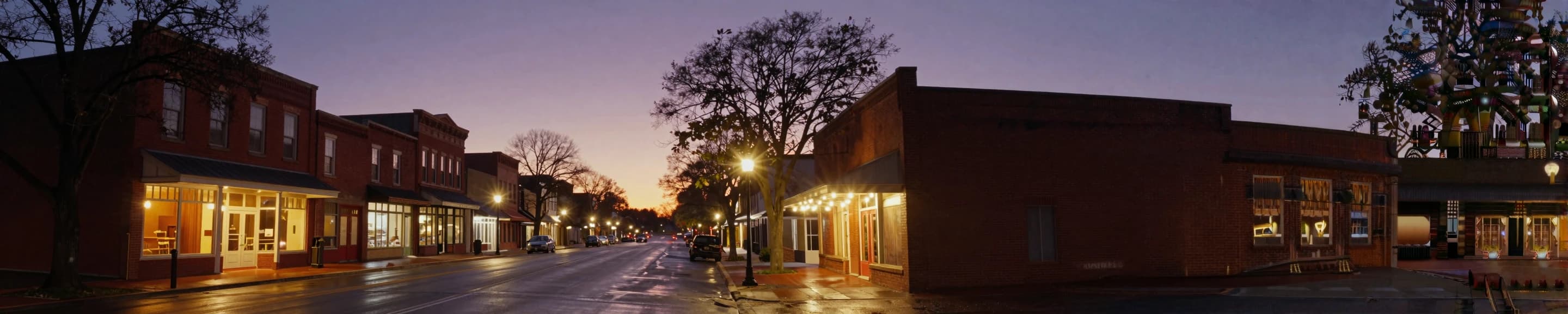 Super-ultrawide brand render: a small North Carolina main street at twilight, brick storefronts lit warm under a purple sky.