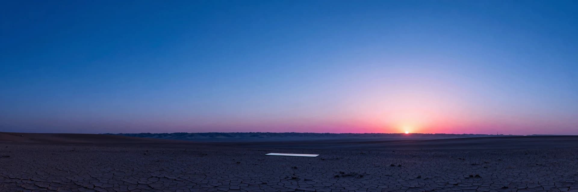 A vast desert basin at golden hour, a single iridescent translucent glass slab tiny in the lower-third of the frame as a small horizontal anchor.