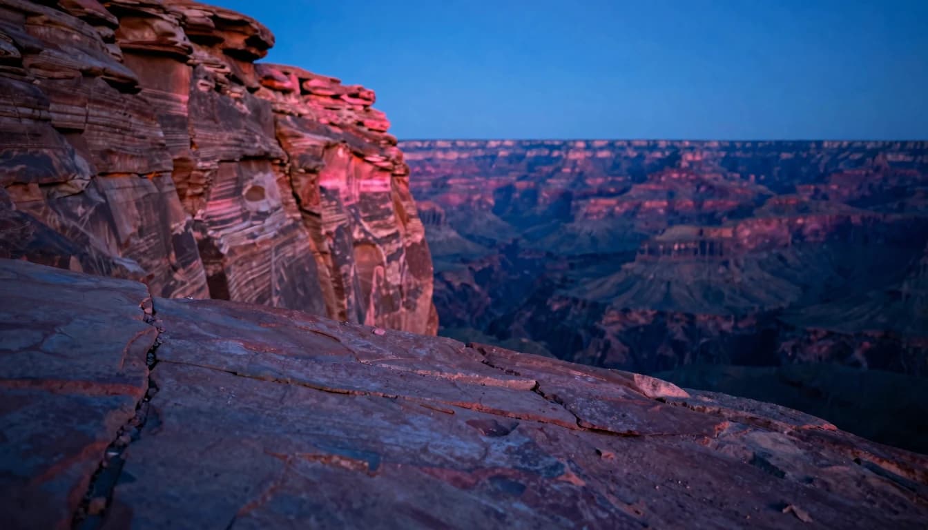 A sandstone canyon with vertical striated walls at dusk, viewed from a foreground canyon rim shelf looking down the corridor, hot-pink glow catching the upper walls.