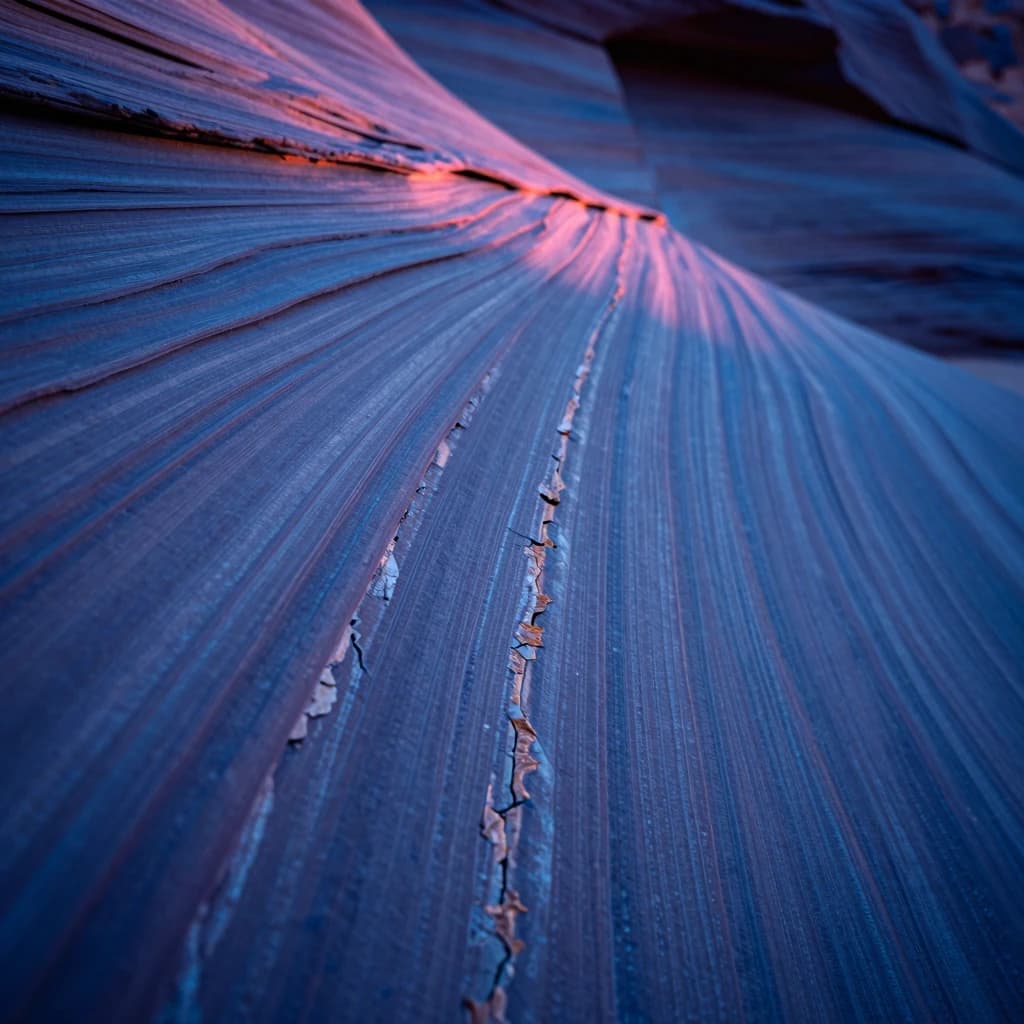 Macro of a sandstone canyon wall with vertical striated formations and mineral staining, electric-blue dusk light grazing from above, hot-pink glow catching the upper striations.