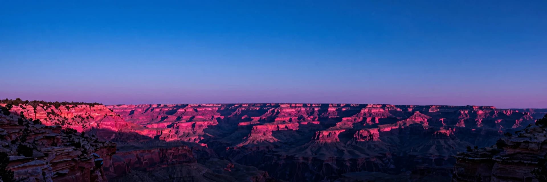 A sandstone canyon ridge silhouette at sunset, the ridge running across the lower third with vertical striated walls visible in profile, hot-pink glow along the entire ridge top.