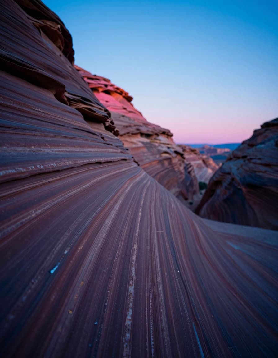 A vertical section of sandstone canyon wall with striated formations running floor to top, mineral staining and thin cracks across the surface, a sliver of electric-blue sky at the upper frame.