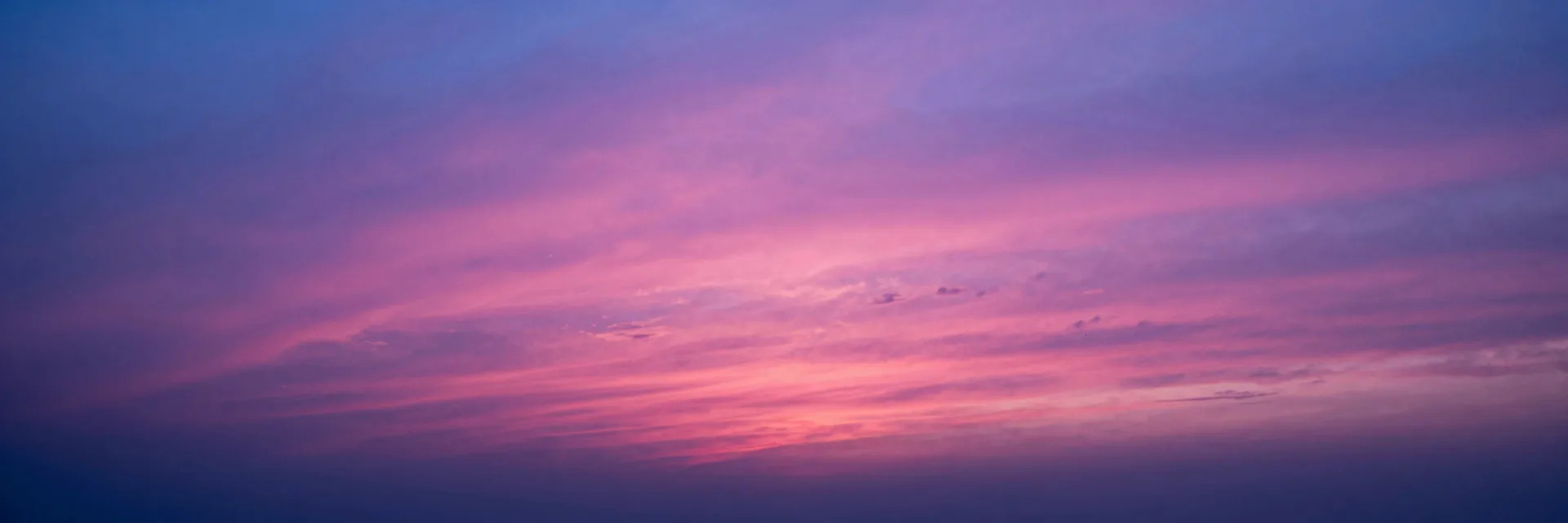 Pure atmospheric photograph of a vibrant pink and purple sunset sky stretching across the entire frame, the sun visible just above the horizon, no rock formation in frame, atmospheric break shot.