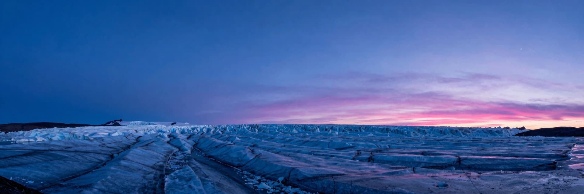 A glacier extending horizontally into the distance at twilight, ice as a low horizontal element across the lower frame, electric-blue twilight sky above, hot-pink alpenglow grazing the upper ice surface.
