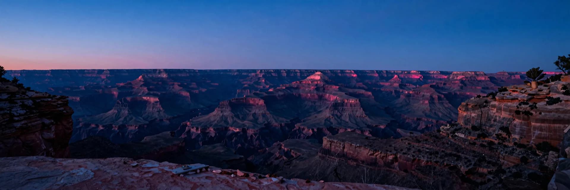 Ultra-wide showing the canyon as a small element within a distant mountain landscape at dusk