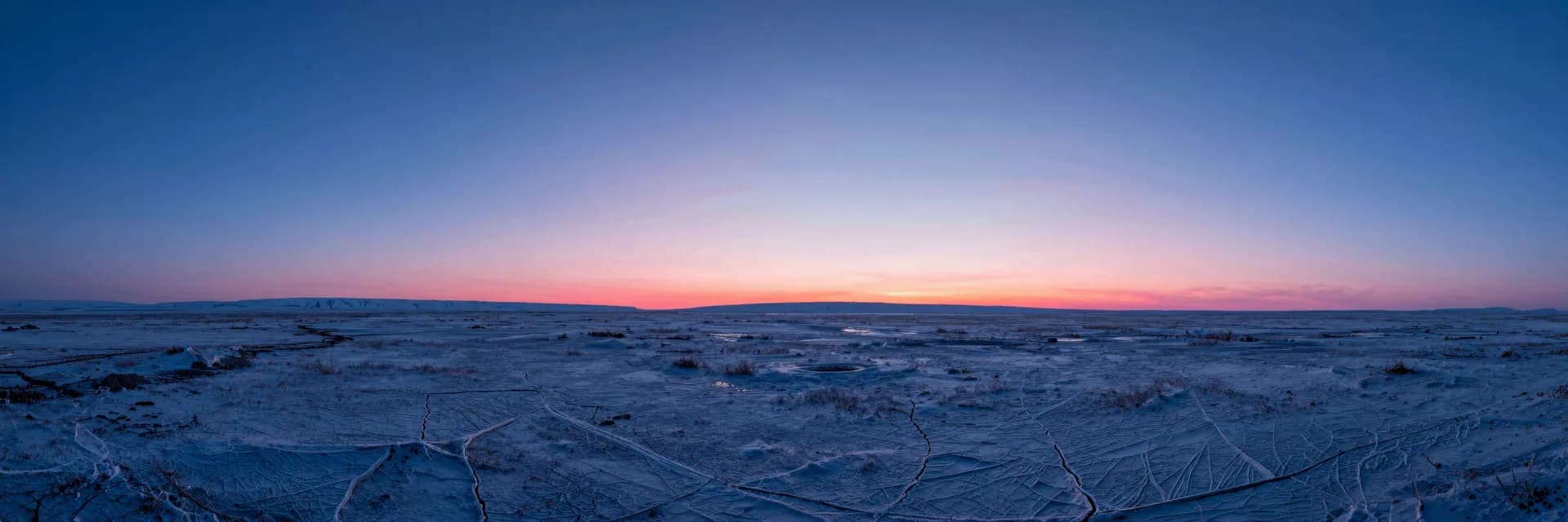 Wide atmospheric landscape at dusk, deep electric blue sky over a quiet plain with a low pink horizon glow softening the foreground.