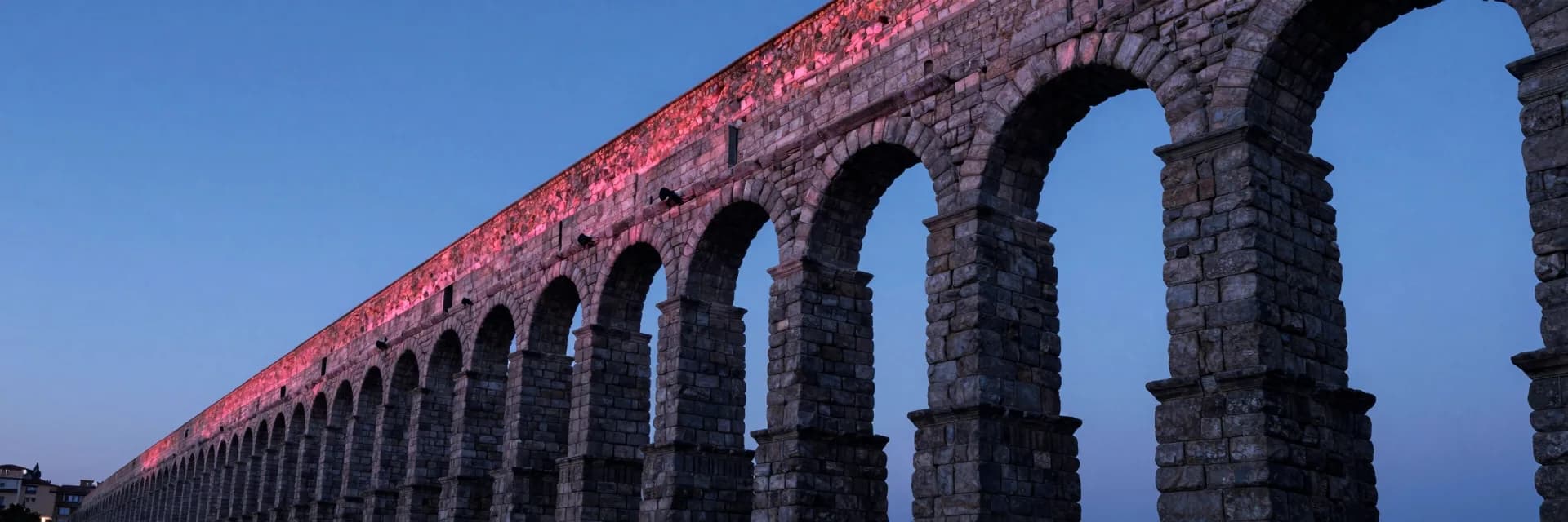 Ultra-wide perspective looking down the length of the stone aqueduct, the row of arches receding to a vanishing point in the distant left third, dramatic perspective leading lines, dawn sky above.
