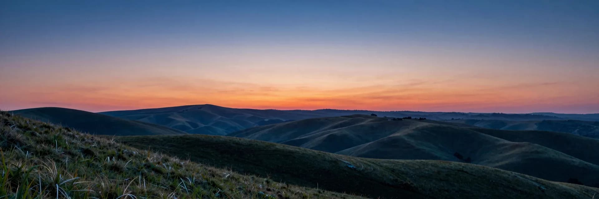 Ultra-wide pure-atmosphere of the pink and orange sunset above rolling hills at last light, no bridge in frame, atmospheric break shot.