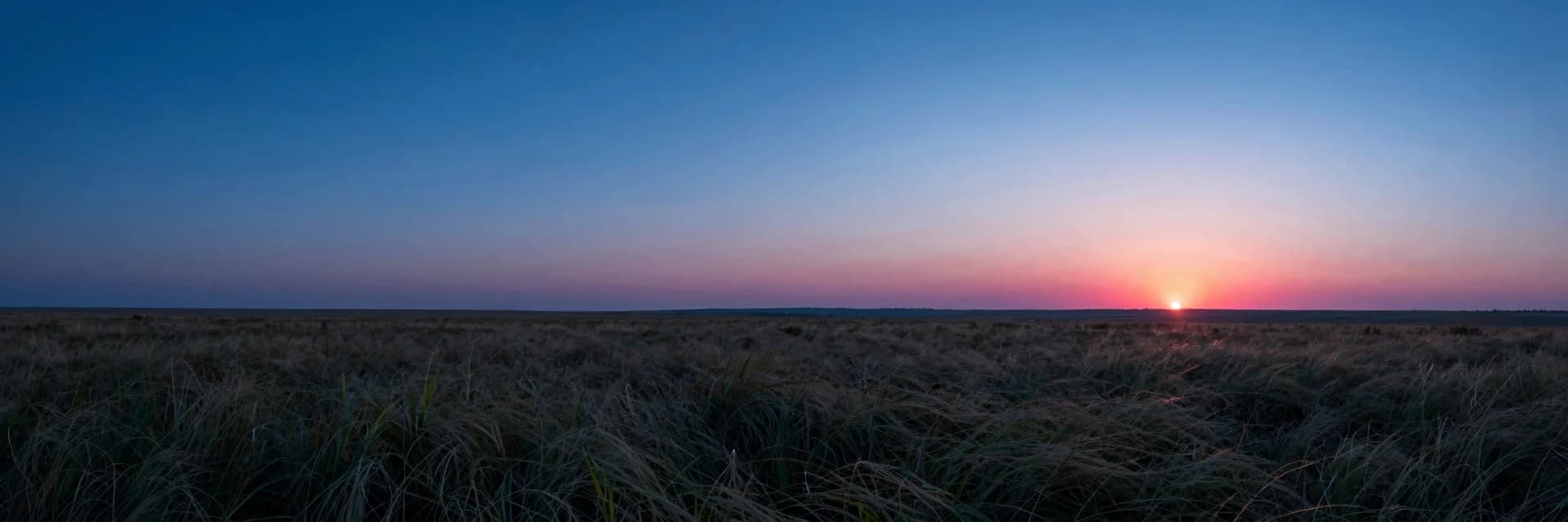 Wide atmospheric scene of layered haze and a single warm horizon line under a deep blue sky.