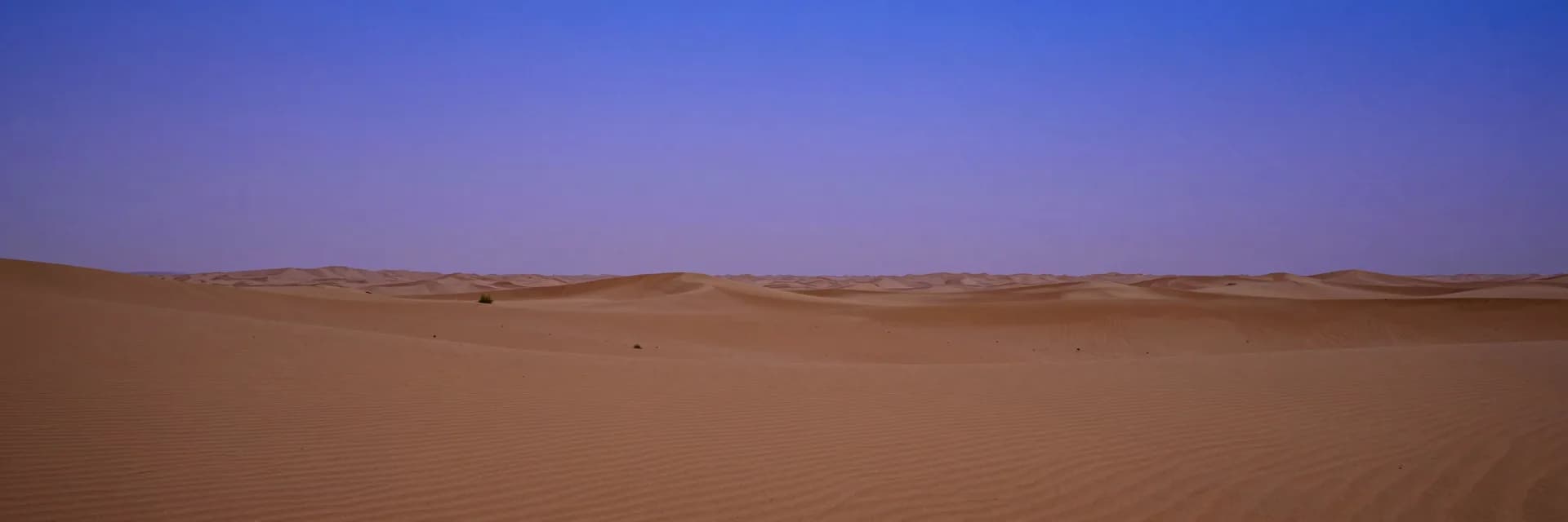 Vast empty desert basin at civil twilight, smooth sand stretching to the horizon
