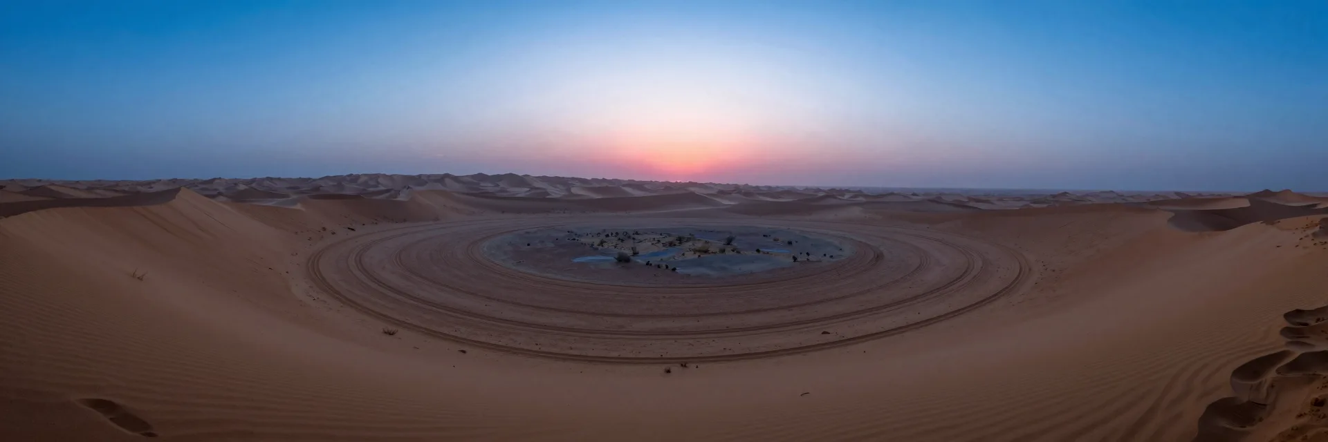 Ultra-wide view of a single ring in a vast desert basin with a sunset along the dune horizon