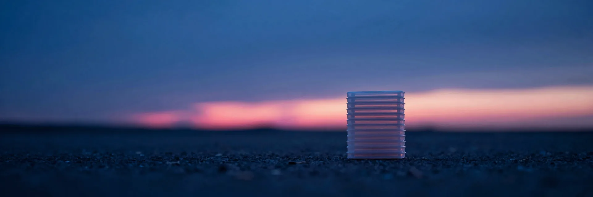 Ultra-wide view of a stack of translucent plastic sheets from a distance, full layered structure visible in soft ambient light.