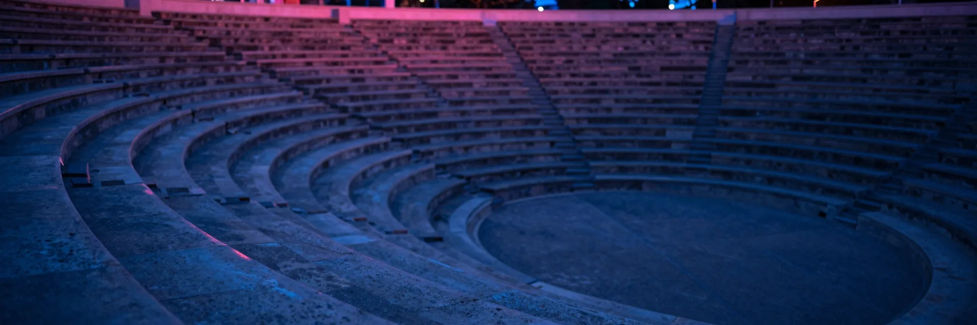 An ultra-wide view of curving tiered stone seats receding to one side along the inside of the amphitheater bowl.