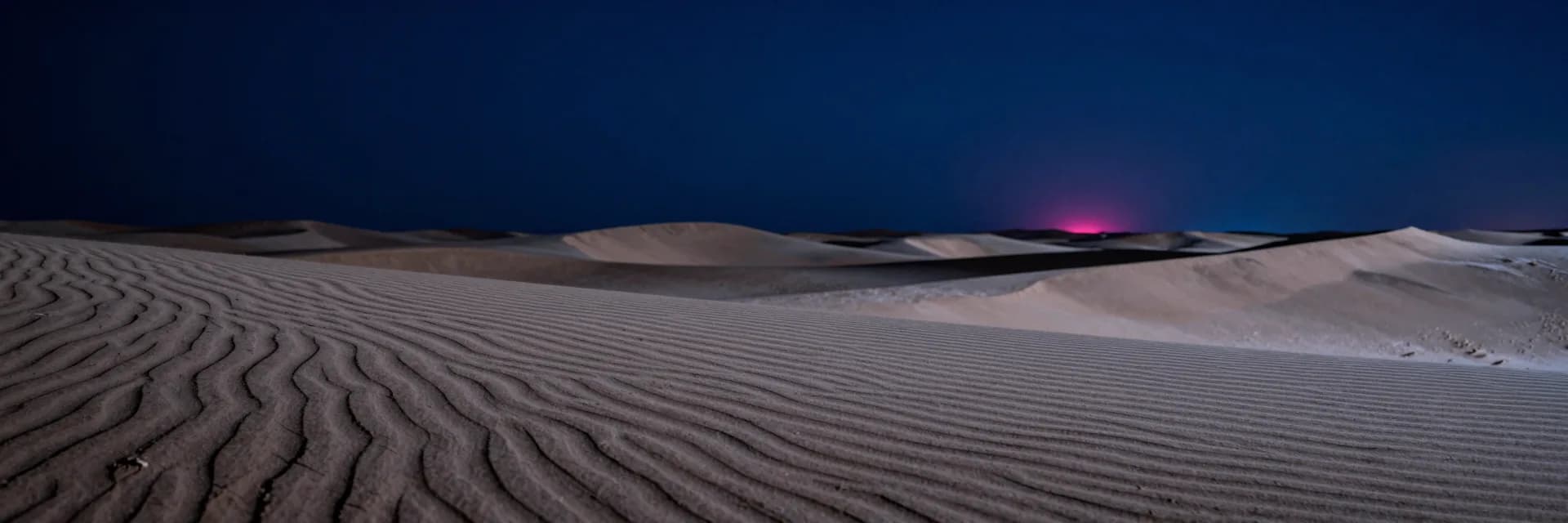 Ultra-wide rippled dunes recede to a vanishing point with dark night sky in the upper portion.
