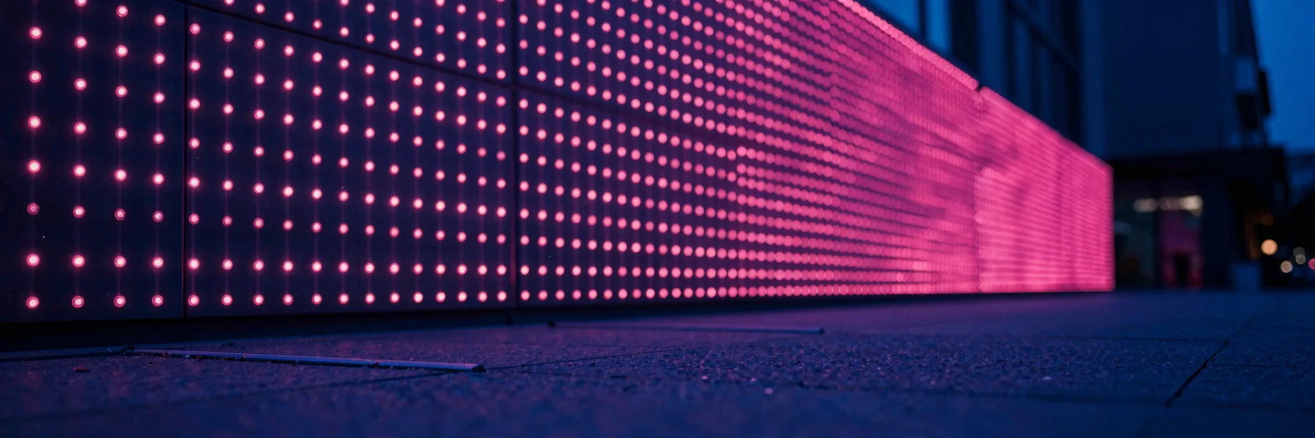 Ultra-wide distant view of the stone corridor showing the full row of hot-pink LEDs as a continuous line.