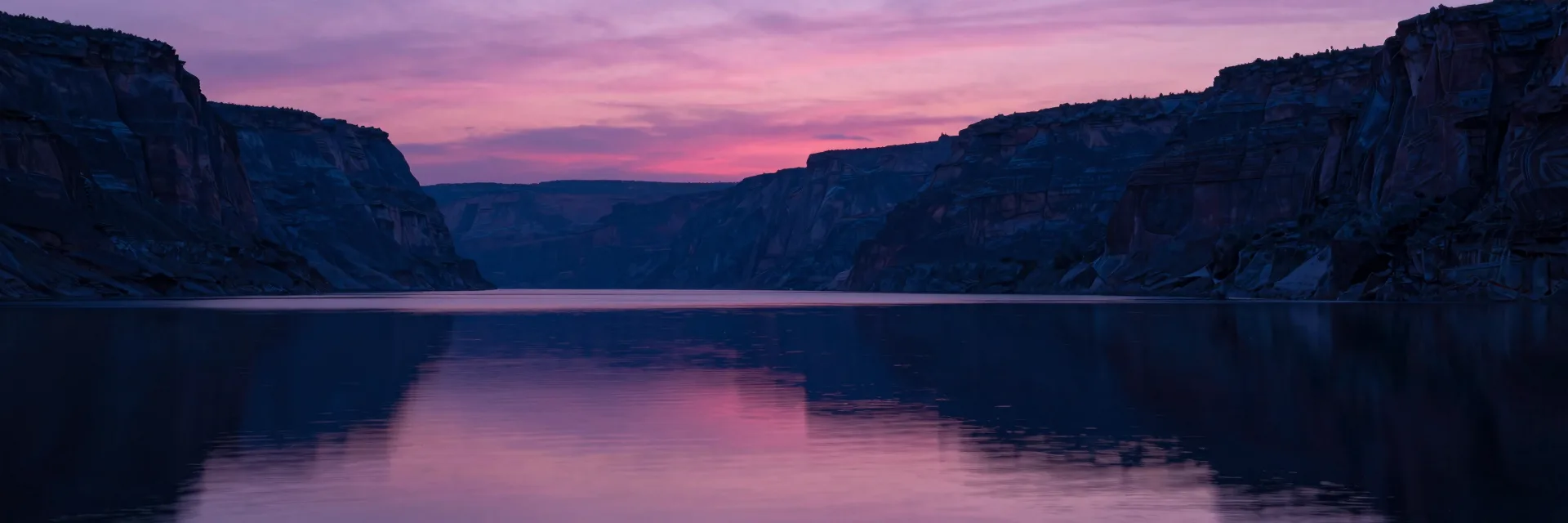 Ultra-wide pure-atmosphere of the calm canyon lake water at last light, the entire frame filled with the smooth reflection of the pink sky and dark canyon walls.