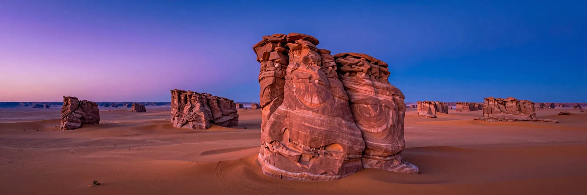 Ultra-wide aerial vista at dusk with the prominent twisted hero hoodoo rooted in the right-third foreground, smaller scattered formations receding into the distance.