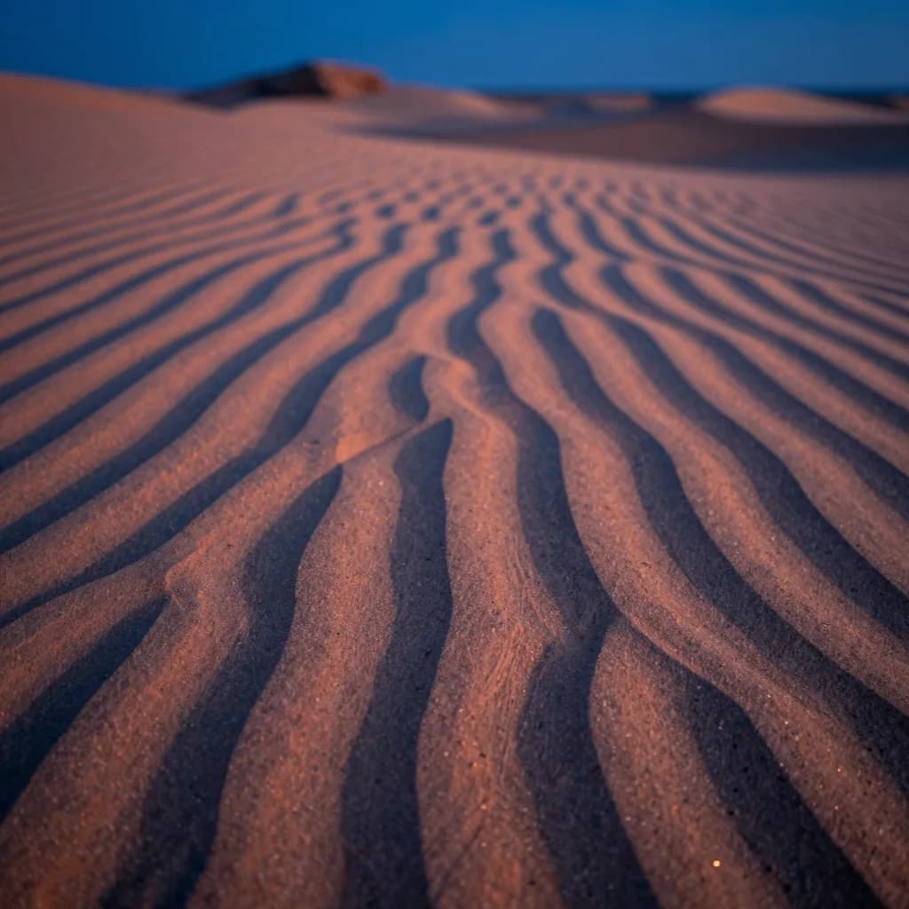 Extreme close-up of orange desert sand showing wind-blown ripple patterns receding to a defocused horizon.