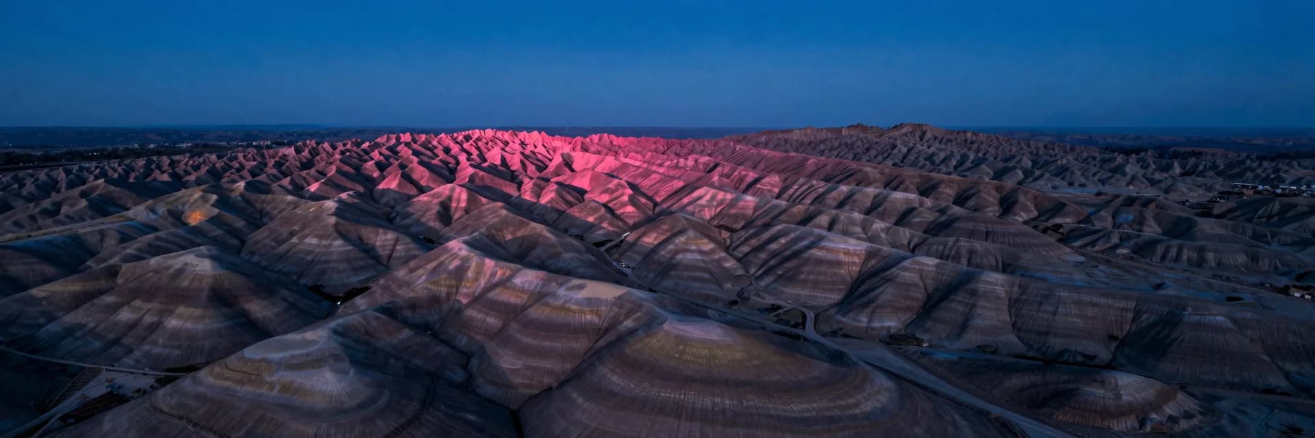 Ultra-wide landscape of rolling colorful eroded hills receding into a distant vanishing point.
