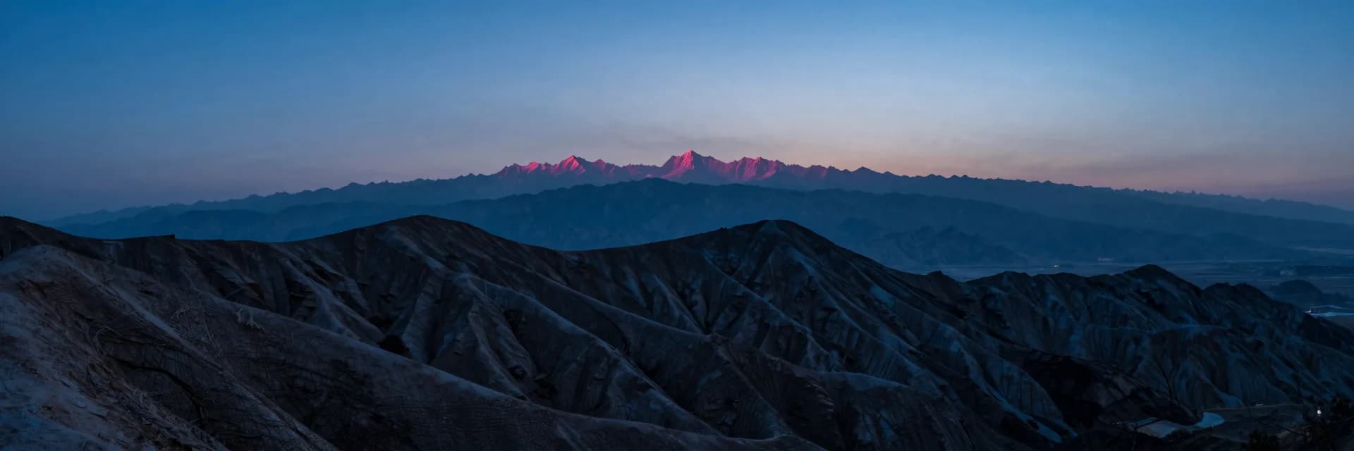 An ultra-wide view of a colorful striated mountain seen from a distant vantage point with dramatic horizontal scale.