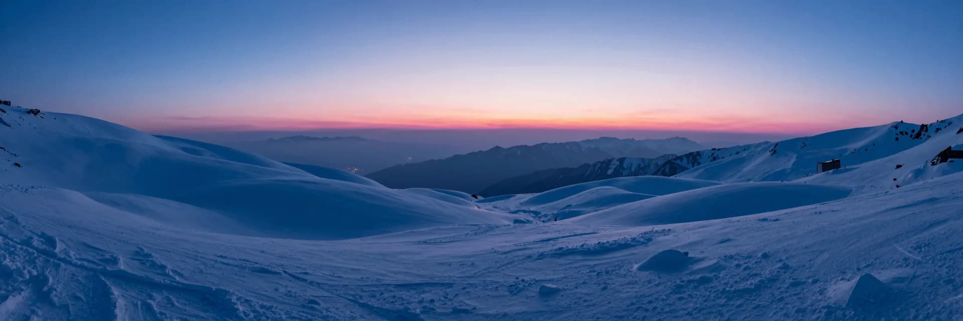 Wide atmospheric landscape at dusk, deep electric blue sky over a quiet plain with a low pink horizon glow softening the foreground.