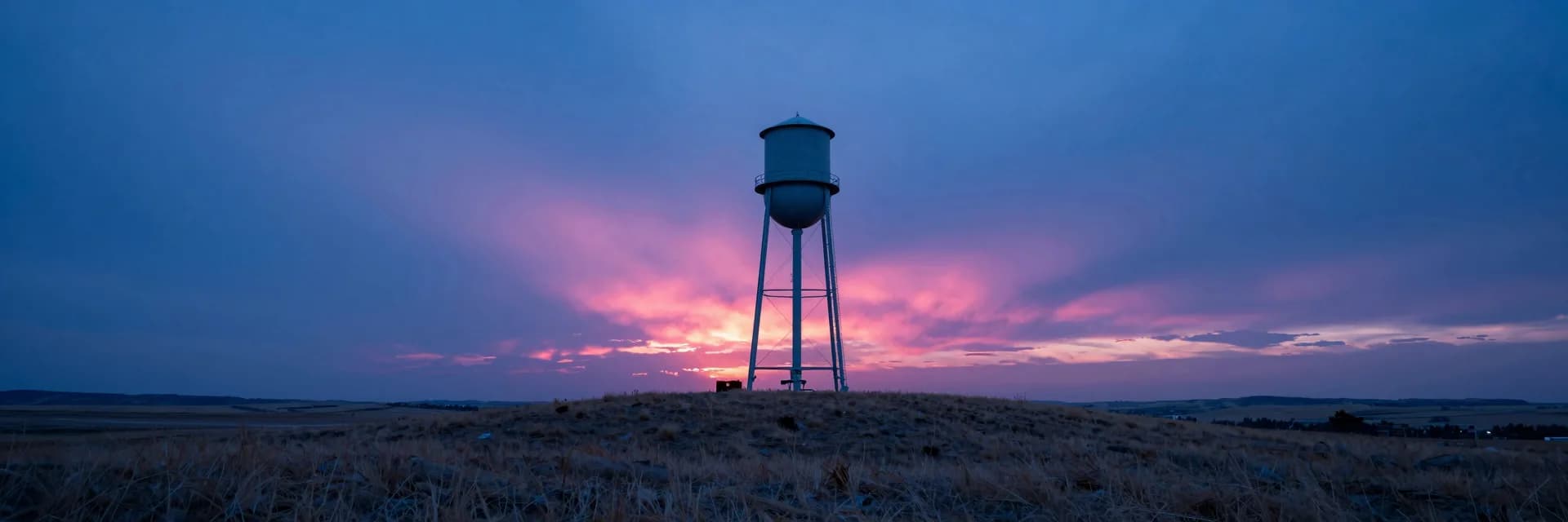 ultra-wide strip of lone industrial silhouette on a prairie at hot-pink sunset - hero image for the retainer trap and why productized beats hours essay