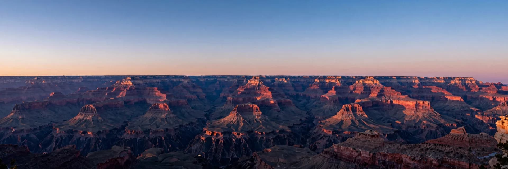 Ultra-wide of the vast Grand Canyon at sunset showing multiple layered ridges receding into atmospheric haze.