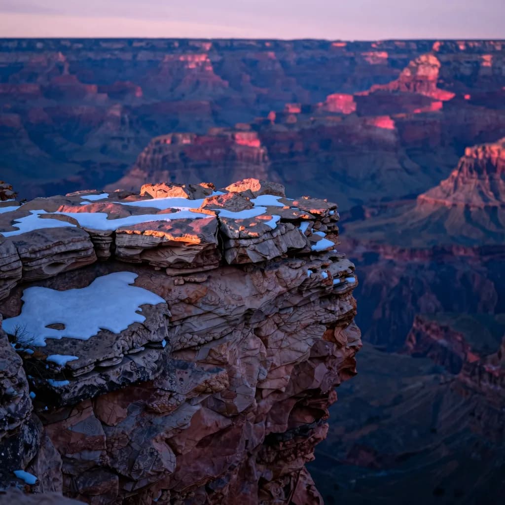 Close-up of a single weathered rock outcropping at the canyon edge at sunset showing layered erosion and snow patches in crevices.