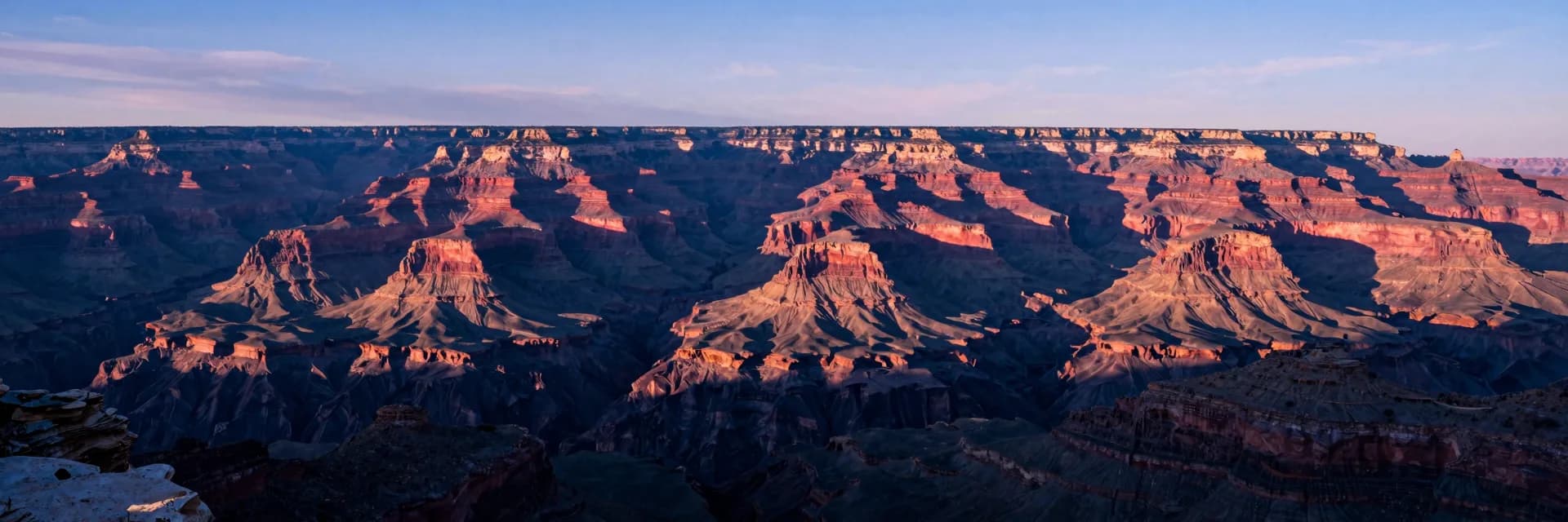 Ultra-wide of the canyon at low golden-hour sun showing dramatic long shadows from canyon walls stretching across the floor below.