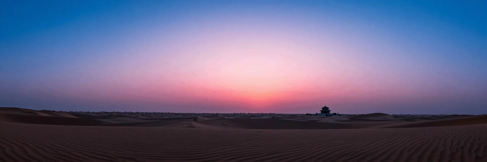 Ultra-wide of the vast empty desert at sunset with the single temple visible as a small silhouette in the right third, dwarfed by empty dunes.