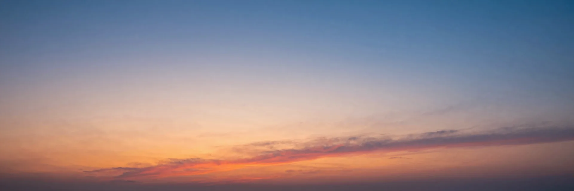 Ultra-wide pure-atmosphere of the gradient sunrise sky transitioning from warm orange and pink near the horizon to cooler blues higher up, no mountains or trees in frame.