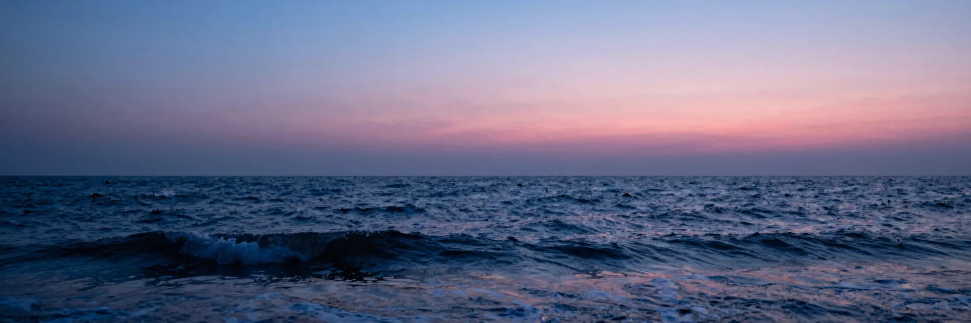 Ultra-wide vast ocean horizon with sculpture small in the landscape at dusk