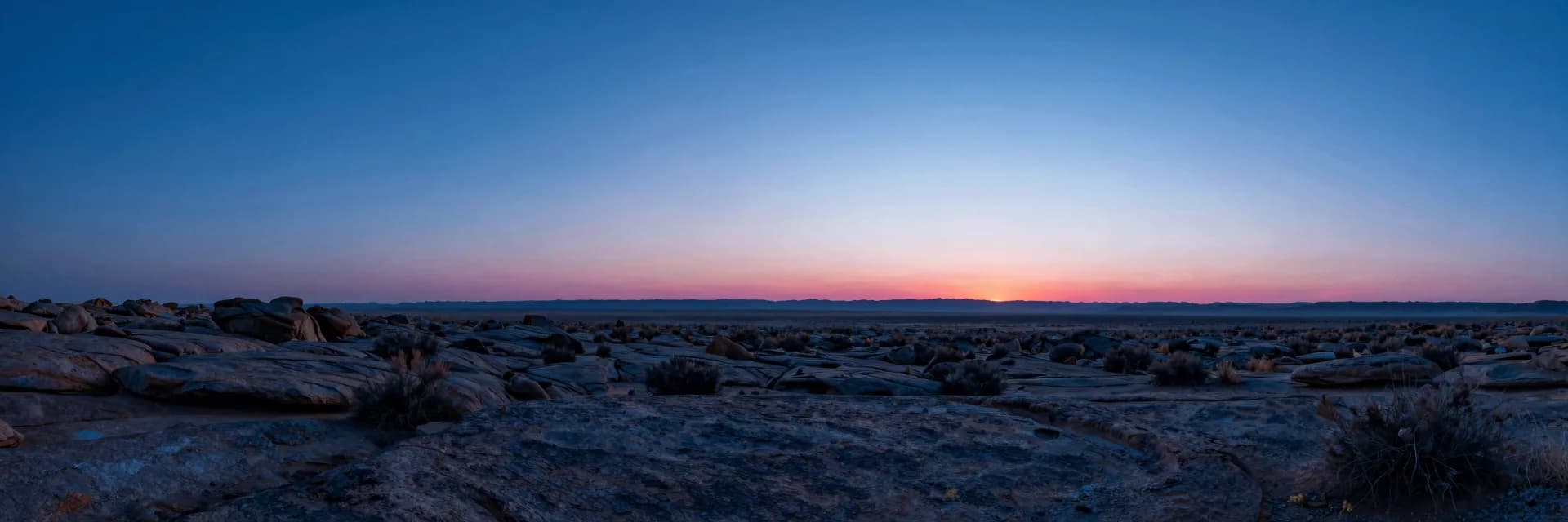 Wide atmospheric scene of deep blue haze layered over a low horizon, single warm point glowing at the far edge.