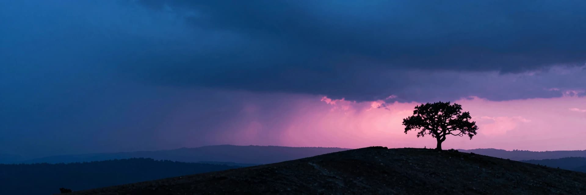 A windswept ridge silhouette at storm break, the ridge running across the lower third, a single lone oak tree in the far-right third, hot-pink sunset break grazing the ridge crest.