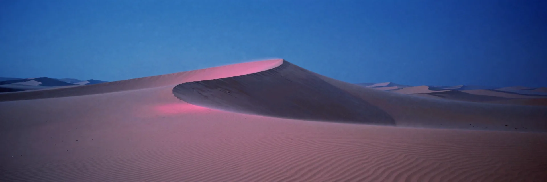 A vast empty dune field stretching wide, a single immense crescent sand dune with rhythmic wind ripples fading to a faint form at the edge of frame.