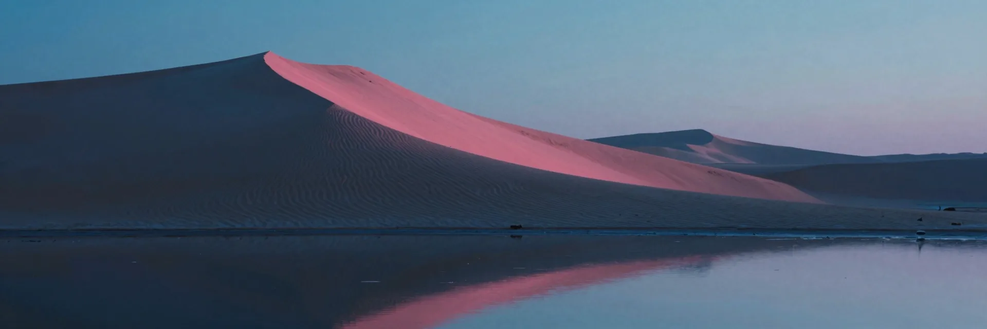A single immense crescent sand dune mirrored on a thin sheen of dawn-wet sabkha at the dune's foot.